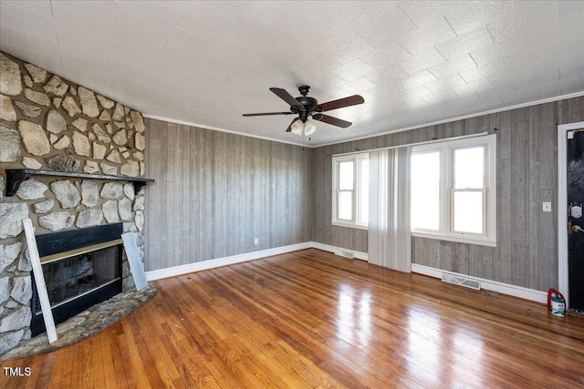 unfurnished living room featuring wood-type flooring, a stone fireplace, ceiling fan, and ornamental molding