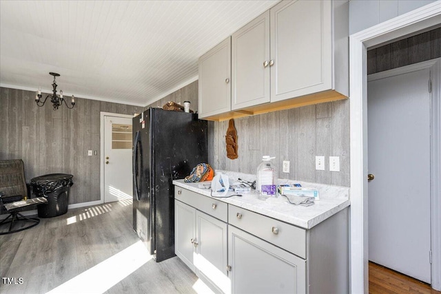 kitchen featuring black fridge, wooden walls, a chandelier, and light wood-type flooring