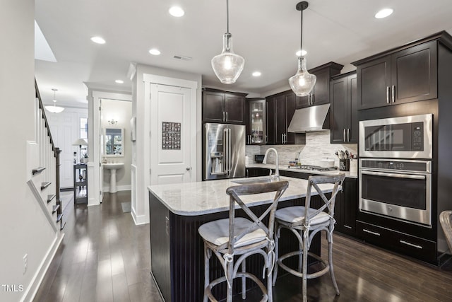 kitchen featuring a kitchen island with sink, decorative light fixtures, light stone counters, dark brown cabinets, and stainless steel appliances