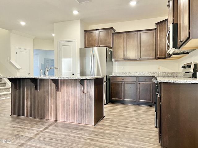 kitchen with light stone counters, light hardwood / wood-style flooring, an island with sink, and stainless steel appliances