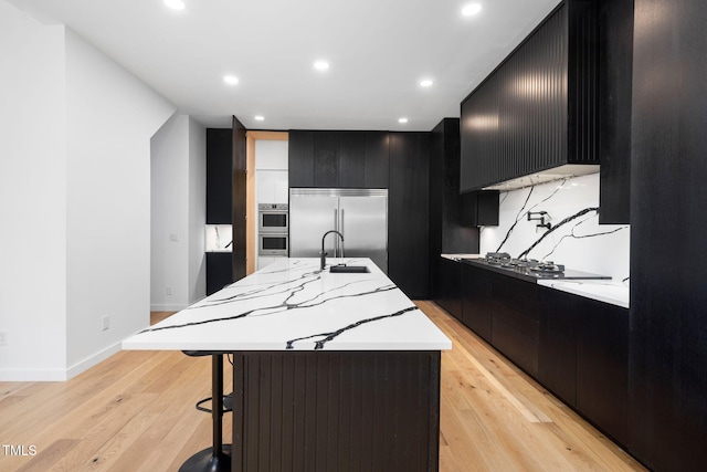 kitchen featuring a breakfast bar, a kitchen island with sink, appliances with stainless steel finishes, and light hardwood / wood-style flooring