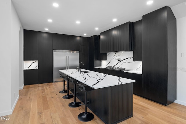 kitchen with a breakfast bar, a center island with sink, built in fridge, sink, and light hardwood / wood-style flooring