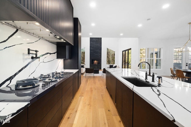 kitchen featuring custom exhaust hood, a high end fireplace, sink, hanging light fixtures, and light hardwood / wood-style floors