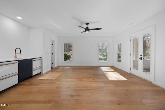 unfurnished living room featuring ceiling fan, light wood-type flooring, sink, and french doors