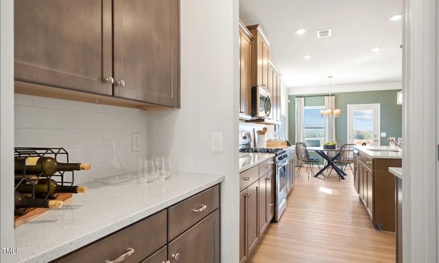 kitchen with light stone countertops, appliances with stainless steel finishes, decorative backsplash, hanging light fixtures, and ornamental molding