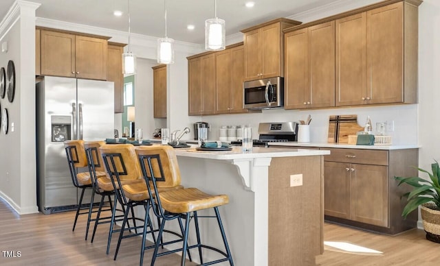 kitchen with decorative light fixtures, light hardwood / wood-style flooring, a kitchen island with sink, appliances with stainless steel finishes, and a kitchen breakfast bar