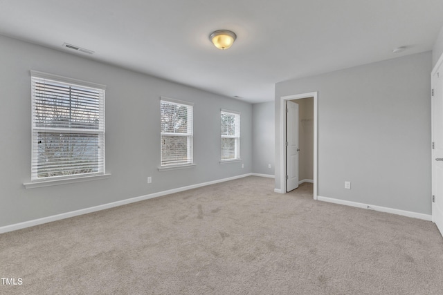 unfurnished bedroom with light carpet, a spacious closet, and multiple windows