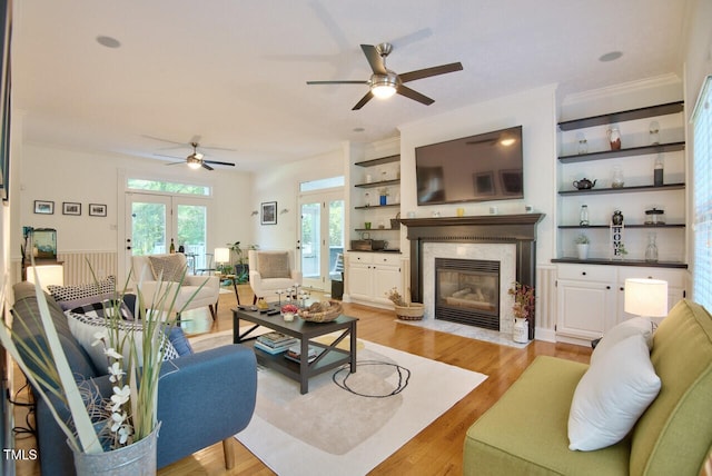 living room featuring ceiling fan, a premium fireplace, light wood-type flooring, ornamental molding, and french doors