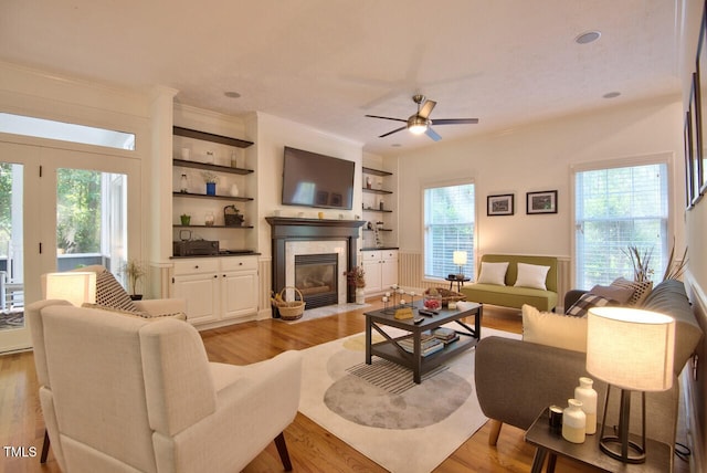 living room featuring ornamental molding, built in shelves, ceiling fan, and light hardwood / wood-style flooring