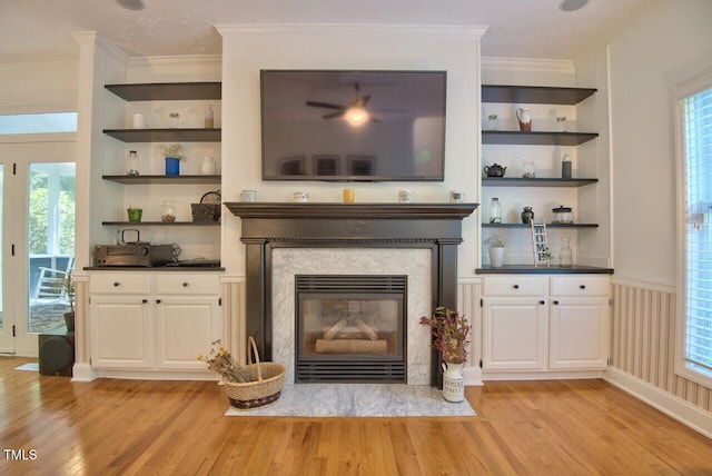 unfurnished living room with ornamental molding, a fireplace with flush hearth, light wood-style flooring, and built in features