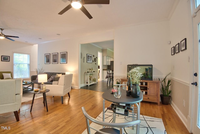 dining space featuring light wood-style floors, a wainscoted wall, crown molding, and a ceiling fan