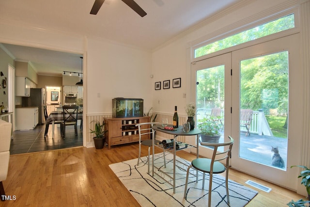 dining room with a wainscoted wall, visible vents, wood finished floors, and ornamental molding