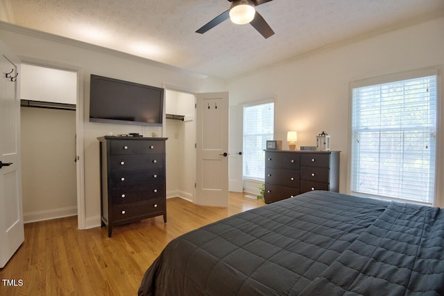 bedroom with two closets, a ceiling fan, a textured ceiling, light wood-type flooring, and baseboards