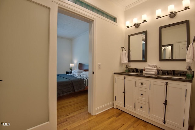 ensuite bathroom with double vanity, crown molding, a sink, and wood finished floors