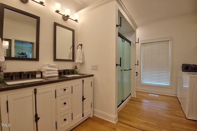 bathroom with ornamental molding, a sink, a shower stall, wood finished floors, and independent washer and dryer