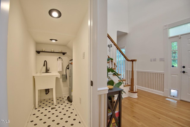 entrance foyer featuring stairs, light wood finished floors, wainscoting, and electric water heater