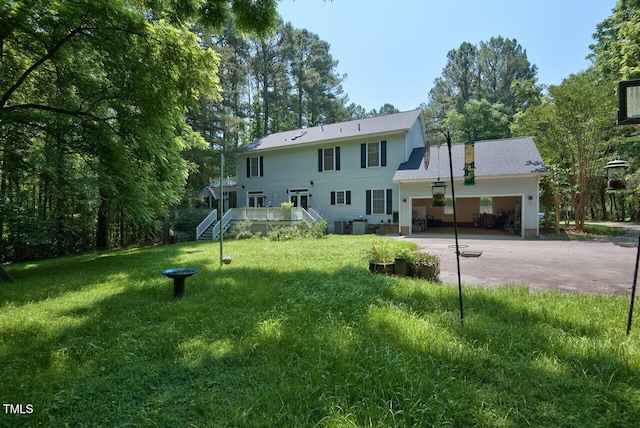 rear view of house with a garage, driveway, a lawn, and stairs