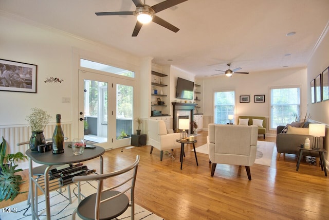 living room with a fireplace, a ceiling fan, ornamental molding, and light wood-type flooring