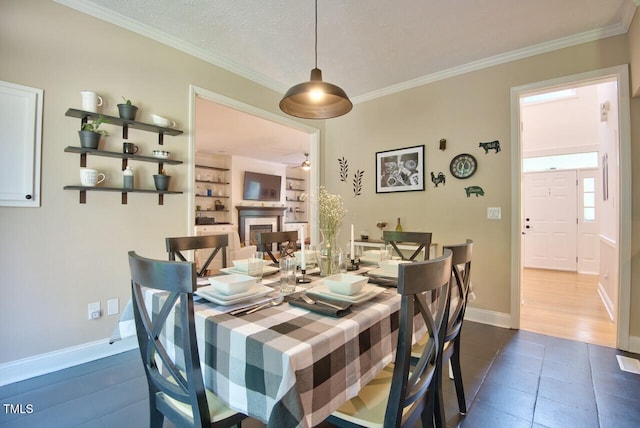 dining room featuring crown molding, a fireplace, baseboards, ceiling fan, and dark tile patterned flooring