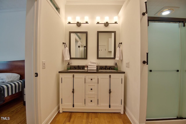 ensuite bathroom featuring double vanity, ornamental molding, wood finished floors, an enclosed shower, and a sink