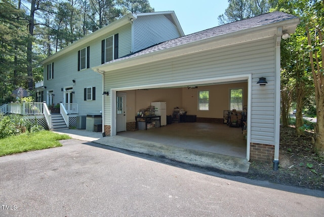 exterior space featuring driveway, a wooden deck, a shingled roof, and cooling unit