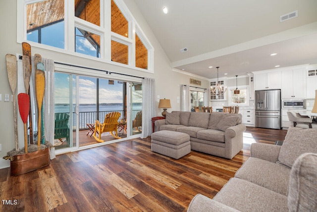 living room with a water view, high vaulted ceiling, dark hardwood / wood-style floors, and a notable chandelier