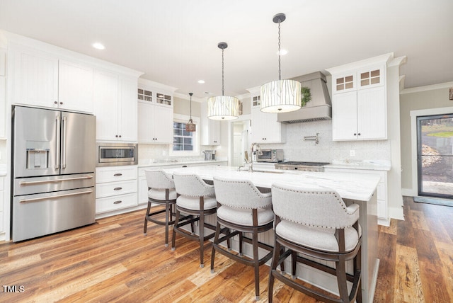 kitchen with white cabinetry, premium range hood, stainless steel appliances, and a kitchen island with sink