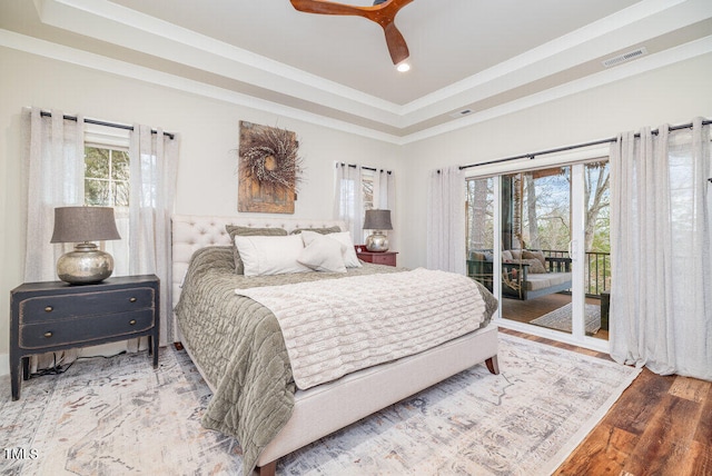 bedroom featuring ceiling fan, a raised ceiling, hardwood / wood-style floors, access to outside, and ornamental molding