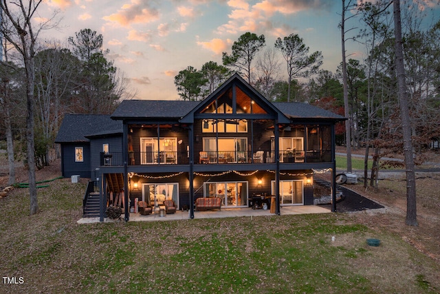 back house at dusk with a wooden deck, a yard, and a patio