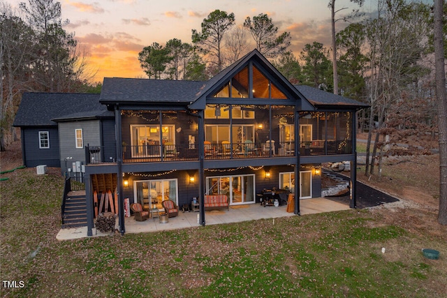 back house at dusk featuring a deck, a patio, and a yard