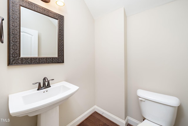 half bathroom with baseboards, a sink, toilet, and wood finished floors