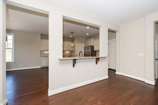 kitchen featuring dark wood finished floors, a breakfast bar area, light stone countertops, fridge with ice dispenser, and pendant lighting