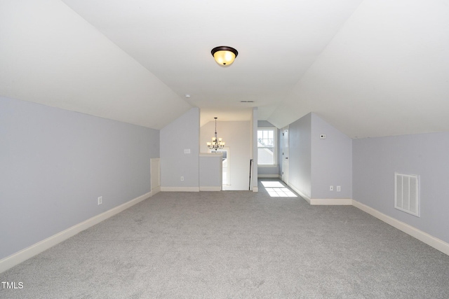 additional living space featuring baseboards, visible vents, light colored carpet, vaulted ceiling, and a chandelier