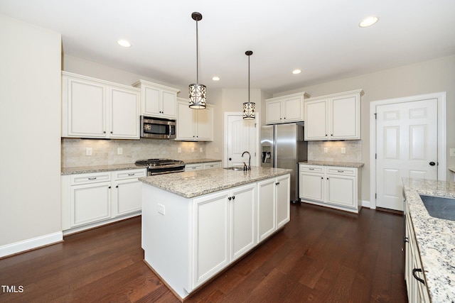 kitchen featuring stainless steel appliances, dark wood-type flooring, light stone countertops, an island with sink, and decorative light fixtures