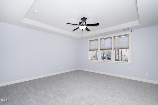 carpeted spare room with a ceiling fan, visible vents, baseboards, ornamental molding, and a tray ceiling