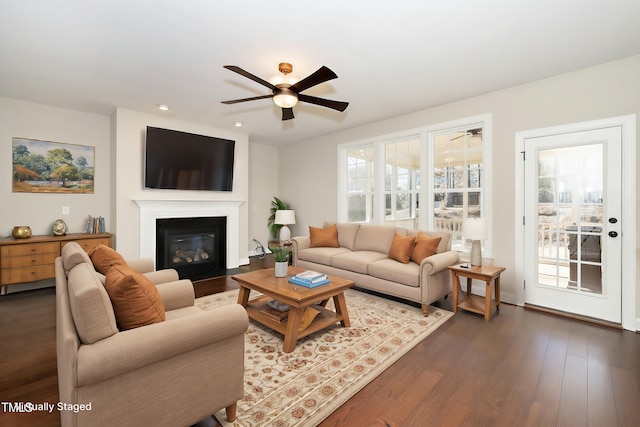 living room with a fireplace with flush hearth, a wealth of natural light, dark wood-style flooring, and ceiling fan