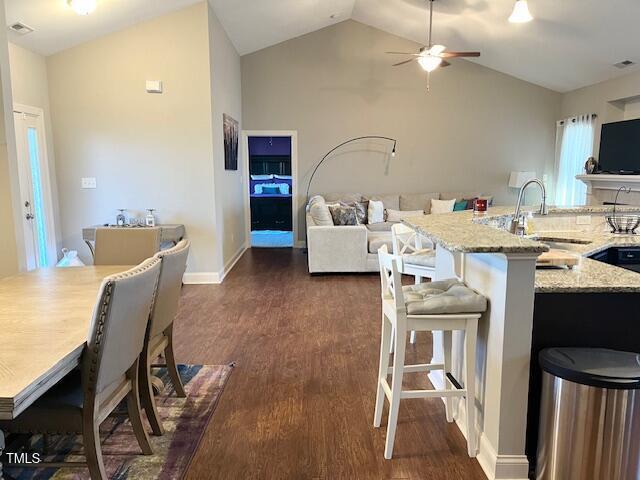 kitchen with a breakfast bar, lofted ceiling, sink, ceiling fan, and light stone counters