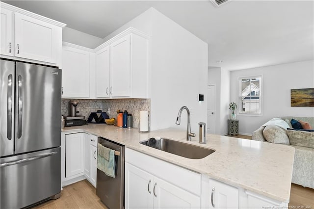 kitchen with white cabinets, appliances with stainless steel finishes, open floor plan, a peninsula, and a sink