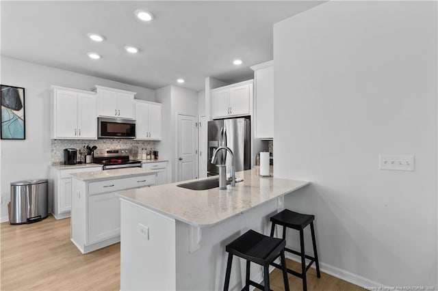 kitchen with white cabinets, a breakfast bar area, a peninsula, stainless steel appliances, and a sink