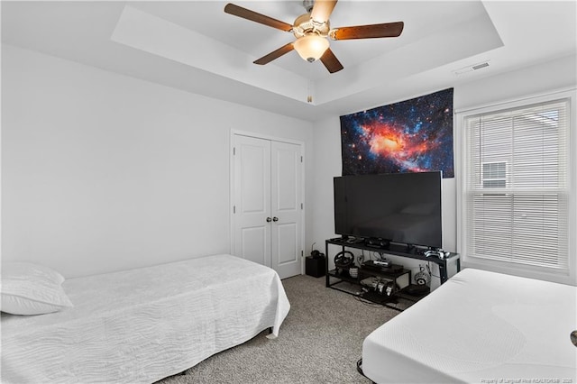 carpeted bedroom featuring a closet, visible vents, a raised ceiling, and a ceiling fan