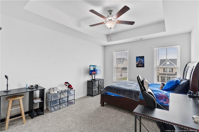 carpeted bedroom with baseboards, a raised ceiling, and a ceiling fan