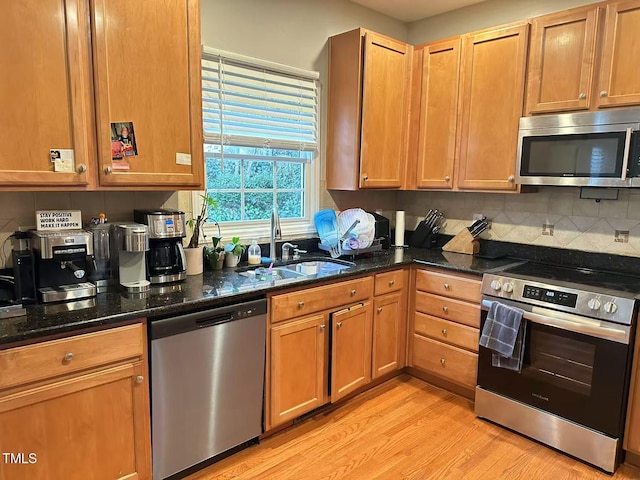 kitchen with tasteful backsplash, sink, dark stone counters, light hardwood / wood-style floors, and stainless steel appliances