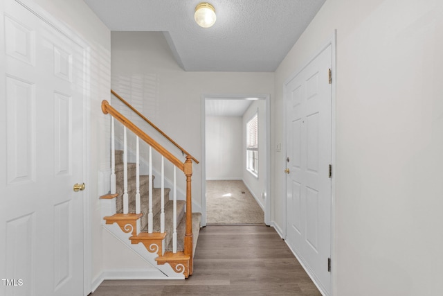 foyer featuring wood finished floors, a textured ceiling, baseboards, and stairs