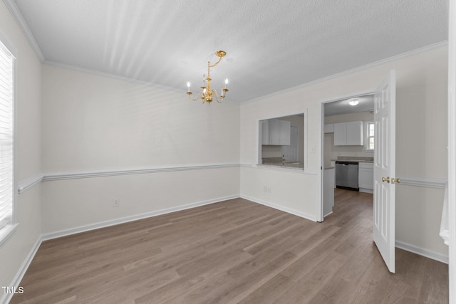 spare room with baseboards, wood finished floors, crown molding, a textured ceiling, and a notable chandelier