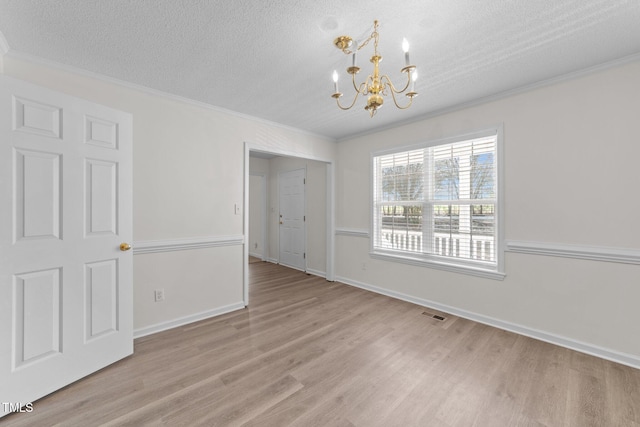 unfurnished dining area with a textured ceiling, ornamental molding, wood finished floors, and an inviting chandelier