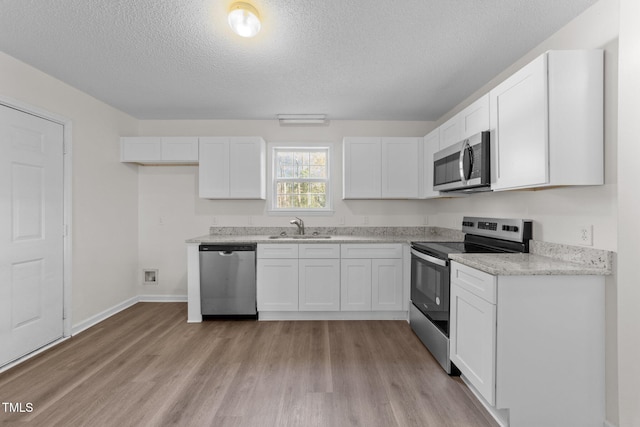 kitchen featuring appliances with stainless steel finishes, a sink, white cabinetry, and light wood-style floors