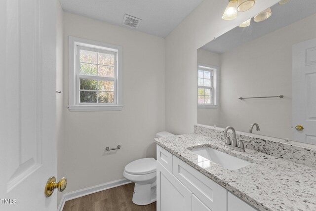 bathroom with baseboards, visible vents, toilet, wood finished floors, and vanity