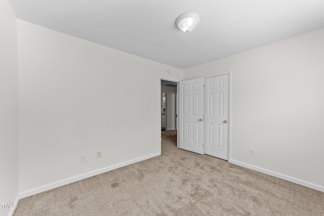 unfurnished bedroom with a textured ceiling, carpet floors, a closet, and baseboards