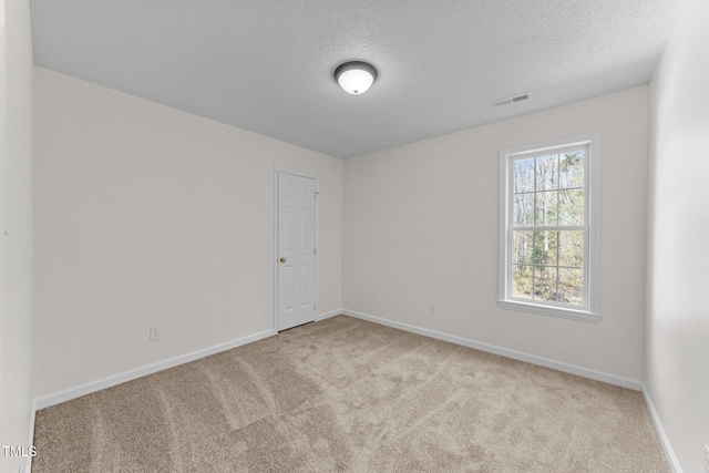 carpeted spare room with visible vents, baseboards, and a textured ceiling