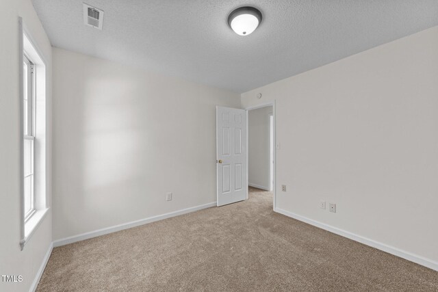 spare room featuring carpet floors, baseboards, visible vents, and a textured ceiling